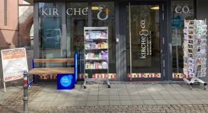 Außenansicht von Kirche & Co in Darmstadt mit Infostand, Flyern und Hinweisschild auf kostenfreie Beratung.