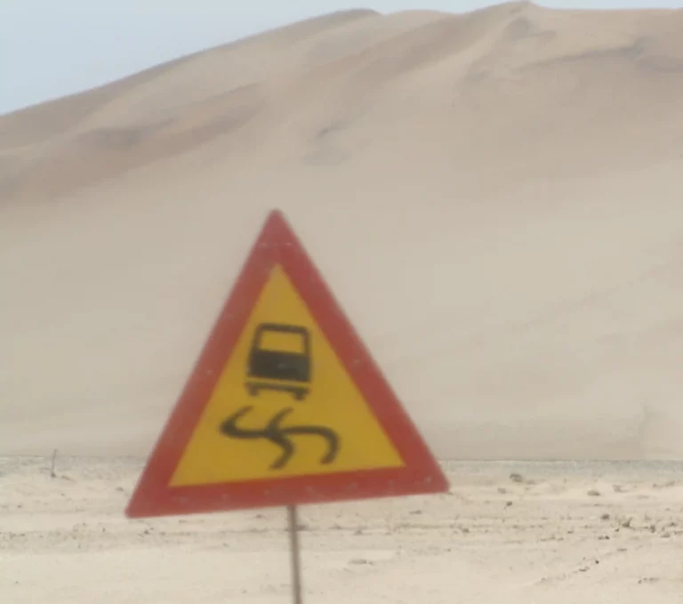 Verkehrsschild „Schleudergefahr“ vor einer Sanddüne in der Wüste